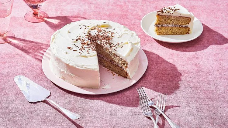 Martha Stewart banana cake with cream-cheese frosting and shaved dark chocolate, with a slice cut out on a pink plate