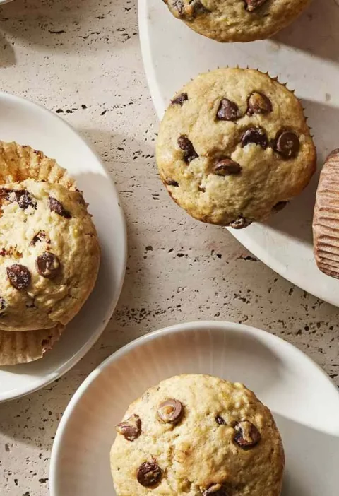 Martha Stewart banana chocolate chip muffins on white plates, one split open to show the tender crumb and melted chocolate chips
