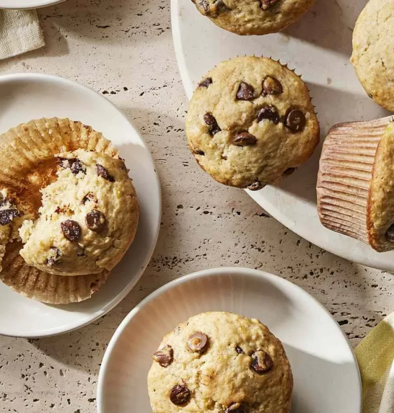 Martha Stewart banana chocolate chip muffins on white plates, one split open to show the tender crumb and melted chocolate chips