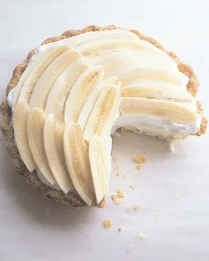 Martha Stewart banana cream pie with overlapping banana slices on whipped cream in a golden crust, with one slice removed