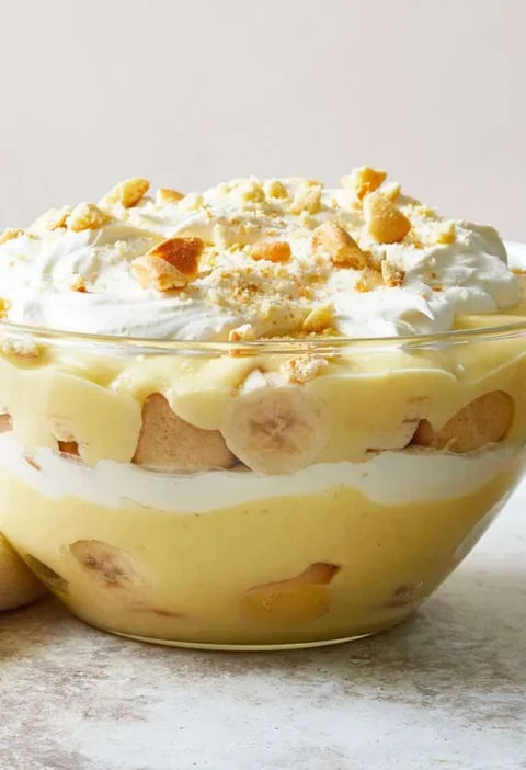 Martha Stewart banana cream pudding layered with custard, banana slices and vanilla wafers in a glass bowl topped with whipped cream and crushed cookies