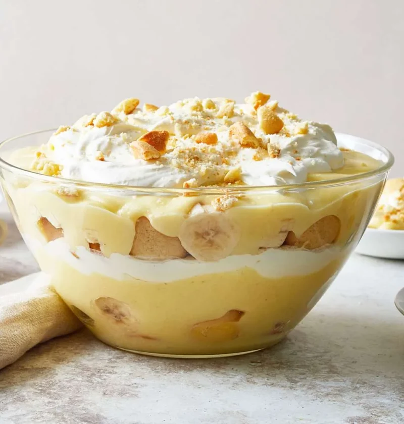 Martha Stewart banana cream pudding layered with custard, banana slices and vanilla wafers in a glass bowl topped with whipped cream and crushed cookies