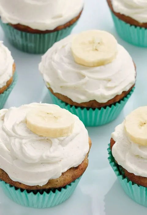 Martha Stewart banana cupcakes with honey-cinnamon frosting and fresh banana slices in teal liners on a white plate