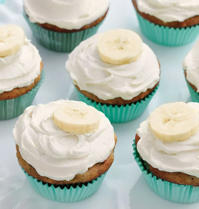 Martha Stewart banana cupcakes with honey-cinnamon frosting and fresh banana slices in teal liners on a white plate