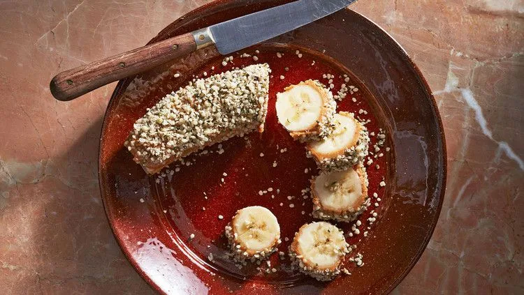 Martha Stewart banana energy bites: a banana coated in nut butter and hemp seeds, sliced into rounds on a brown plate with a knife