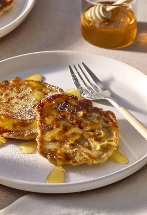 Martha Stewart banana fritters on a white plate drizzled with honey, next to glasses of orange juice