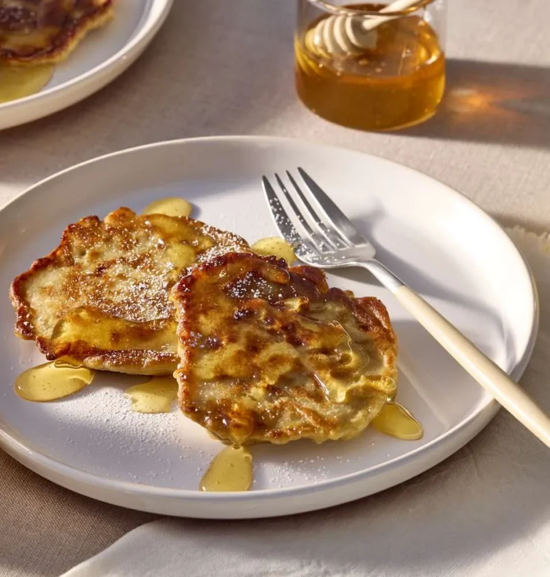 Martha Stewart banana fritters on a white plate drizzled with honey, next to glasses of orange juice