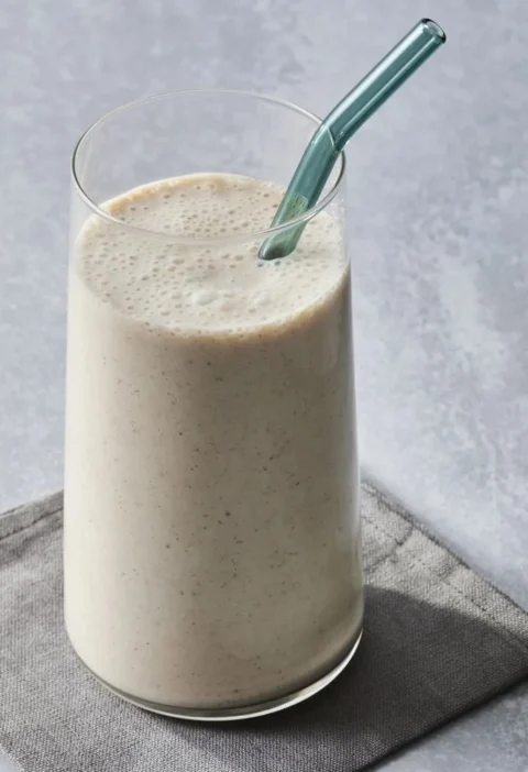 Martha Stewart banana-oat smoothie in a tall glass with a teal glass straw on a gray linen napkin