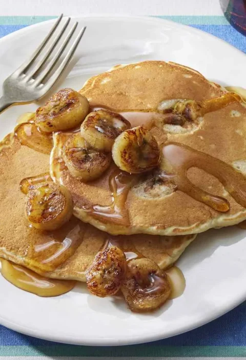 Martha Stewart banana pancakes topped with caramelized banana slices and syrup on a white plate with a fork