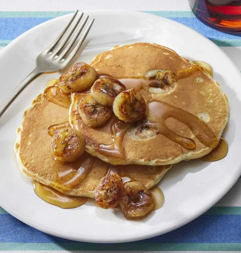 Martha Stewart banana pancakes topped with caramelized banana slices and syrup on a white plate with a fork