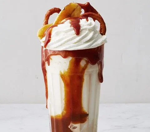 Martha Stewart bananas foster milkshake in a tall glass with caramel drizzle, whipped cream and caramelized banana on top