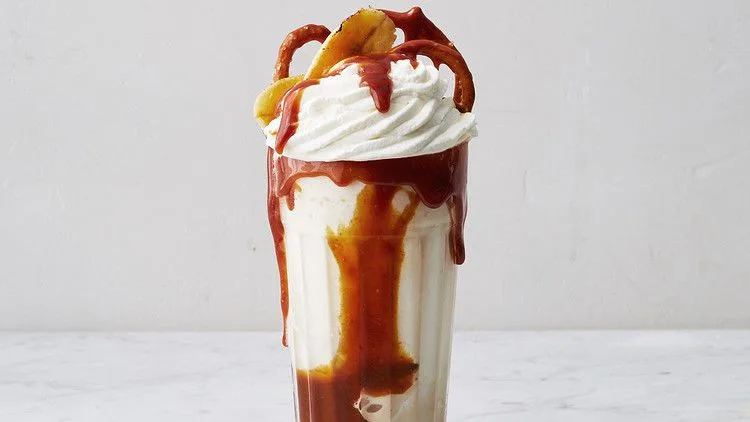 Martha Stewart bananas foster milkshake in a tall glass with caramel drizzle, whipped cream and caramelized banana on top