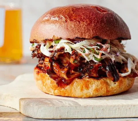 Martha Stewart barbecue pulled mushroom sandwich on a brioche bun topped with slaw, served next to a glass of beer