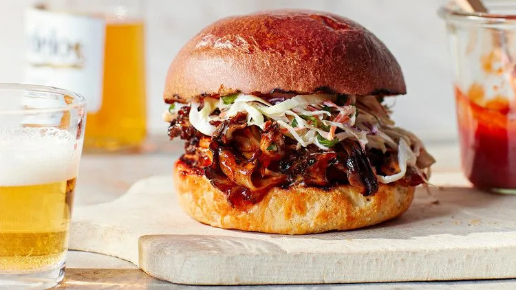 Martha Stewart barbecue pulled mushroom sandwich on a brioche bun topped with slaw, served next to a glass of beer