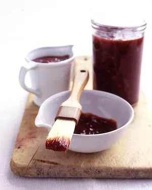 Martha Stewart barbecue sauce in a glass jar, a small bowl with a basting brush and a white pitcher on a wooden board