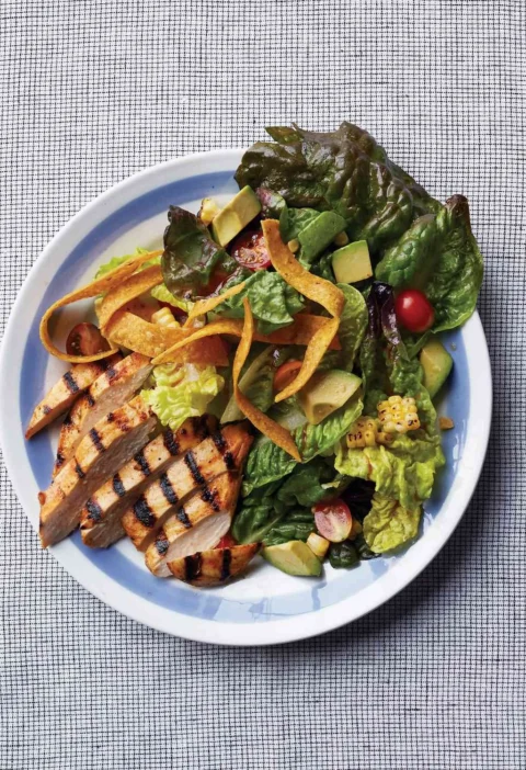 Martha Stewart barbecued-chicken salad with sliced grilled chicken, avocado, cherry tomatoes, charred corn and tortilla strips on a blue-rimmed plate