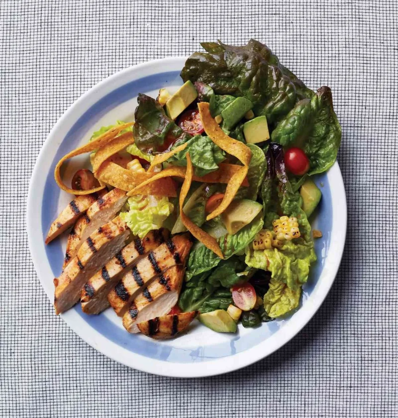Martha Stewart barbecued-chicken salad with sliced grilled chicken, avocado, cherry tomatoes, charred corn and tortilla strips on a blue-rimmed plate
