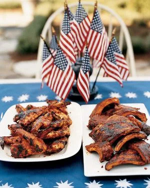 Martha Stewart barbecued chicken wings and ribs on white platters beside small American flags on a blue star tablecloth