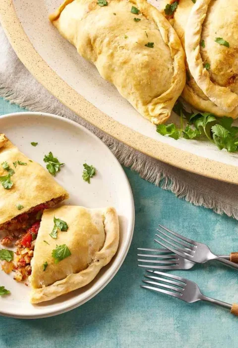 Martha Stewart basic empanadas baked golden with crimped edges, one cut open to show the spiced meat filling, topped with fresh cilantro