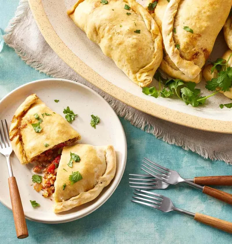 Martha Stewart basic empanadas baked golden with crimped edges, one cut open to show the spiced meat filling, topped with fresh cilantro
