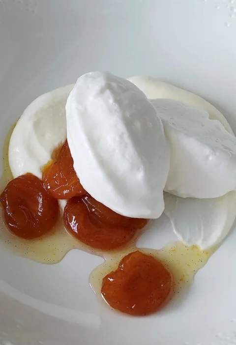 Martha Stewart basic French meringue shaped into glossy quenelles on a white plate with cream and apricots