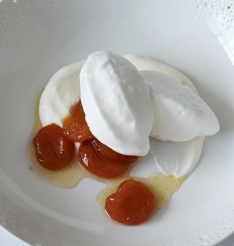 Martha Stewart basic French meringue shaped into glossy quenelles on a white plate with cream and apricots