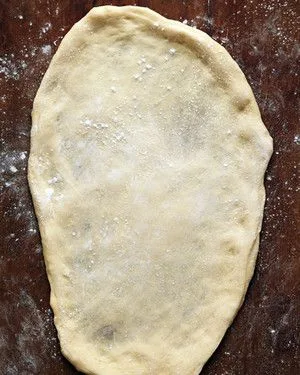 Stretched oval of Martha Stewart basic grilled pizza dough on a floured dark wooden surface