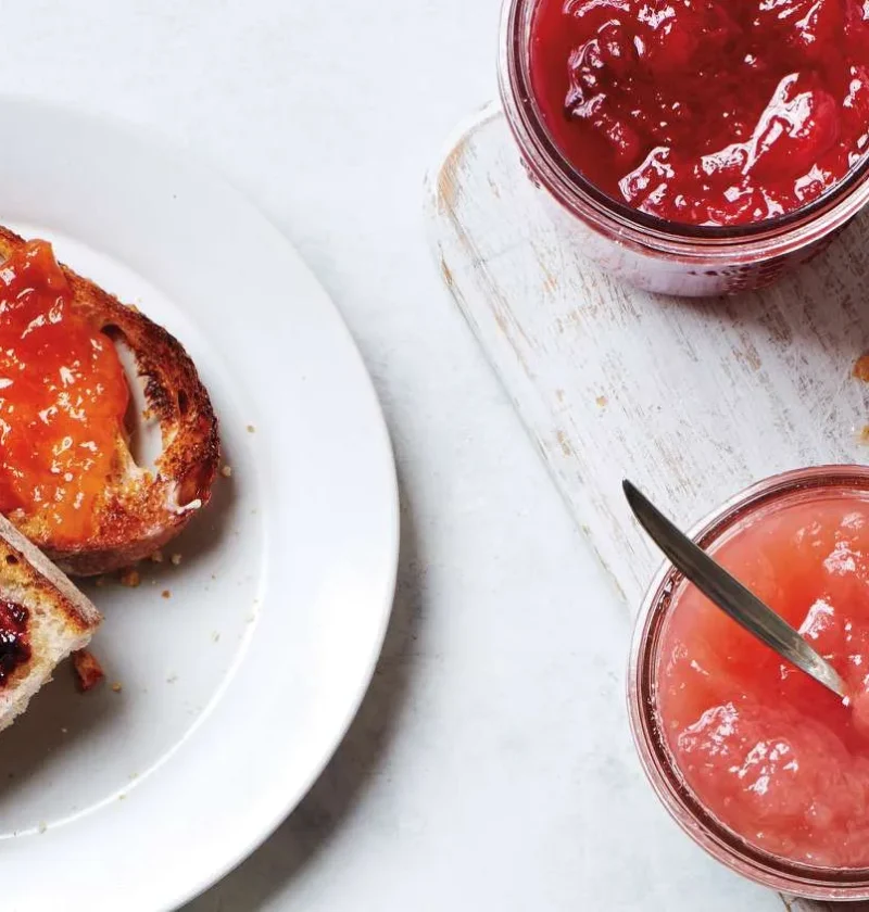 Martha Stewart basic jam in glass jars next to toast spread with orange and blackberry jam
