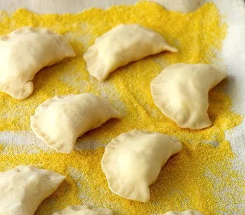 Martha Stewart basic pierogi shaped into crescents resting on a cornmeal-dusted linen towel on a baking sheet