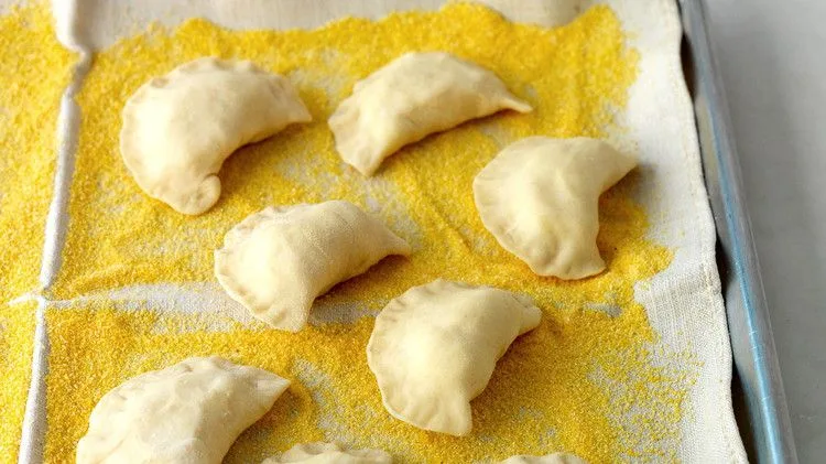 Martha Stewart basic pierogi shaped into crescents resting on a cornmeal-dusted linen towel on a baking sheet