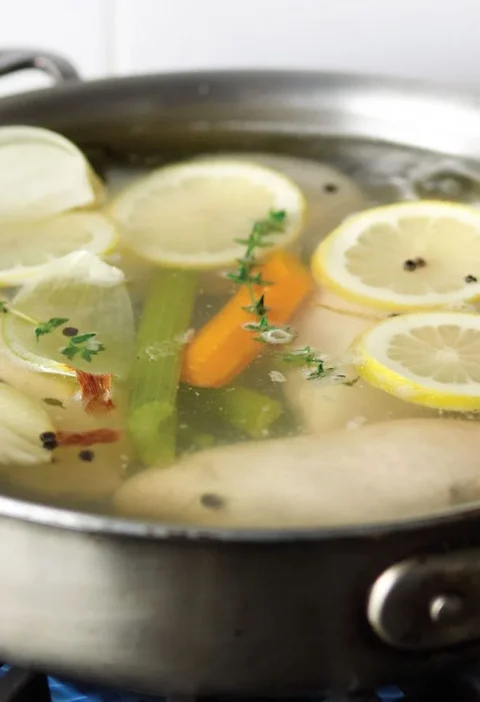 Martha Stewart basic poached chicken breasts simmering in a skillet with lemon slices, carrot, celery, onion and thyme