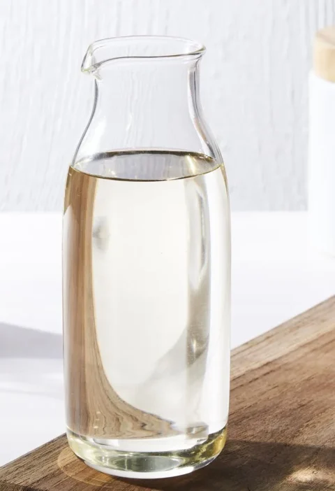 Martha Stewart basic simple syrup in a clear glass carafe next to a jar of sugar on a wooden cutting board