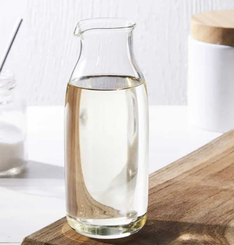 Martha Stewart basic simple syrup in a clear glass carafe next to a jar of sugar on a wooden cutting board