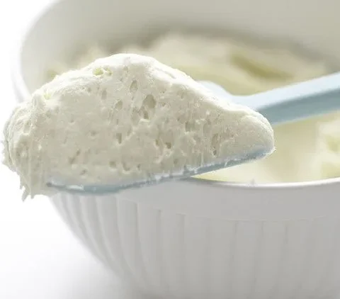 Martha Stewart basic vanilla buttercream on a light blue spatula above a white mixing bowl of fluffy frosting