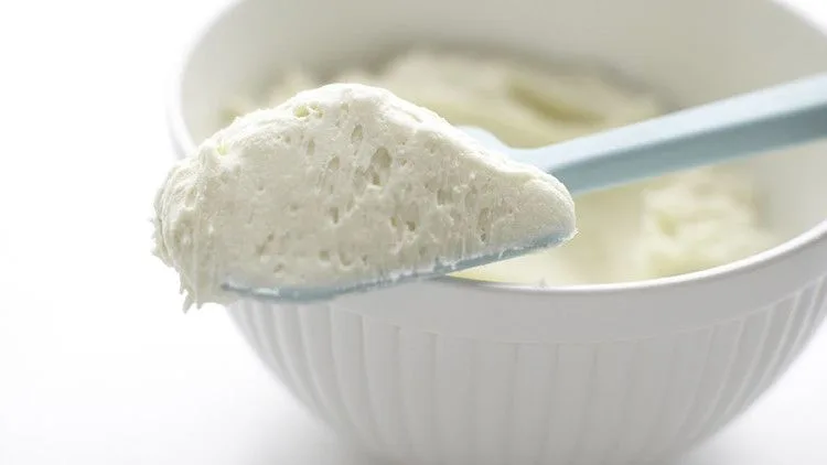 Martha Stewart basic vanilla buttercream on a light blue spatula above a white mixing bowl of fluffy frosting