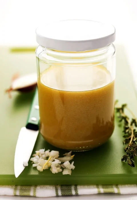 Martha Stewart basic vinaigrette in a glass jar with minced shallot, a fresh thyme sprig and a paring knife on a green cutting board