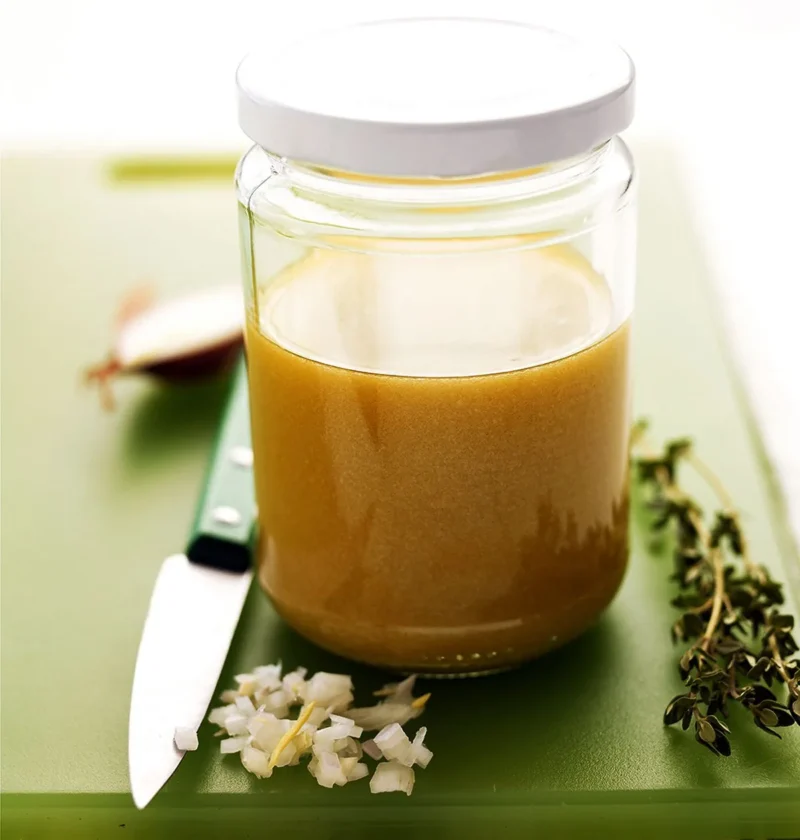 Martha Stewart basic vinaigrette in a glass jar with minced shallot, a fresh thyme sprig and a paring knife on a green cutting board