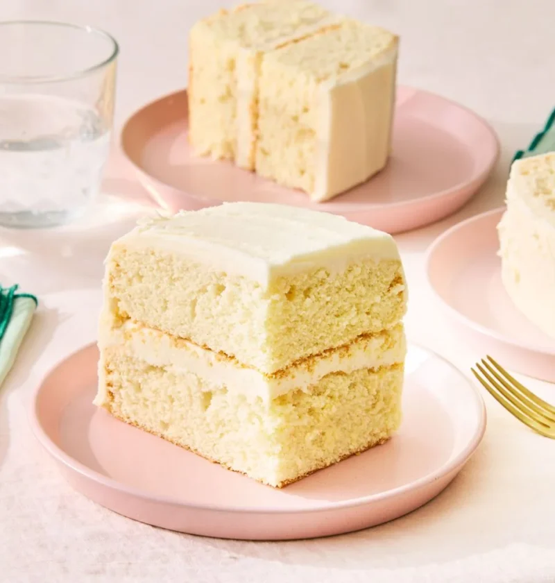 Martha Stewart basic white sheet cake sliced into two-layer pieces with vanilla frosting on pink plates