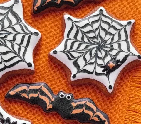 Martha Stewart bat and cobweb Halloween cookies decorated with black and white royal icing on an orange cloth