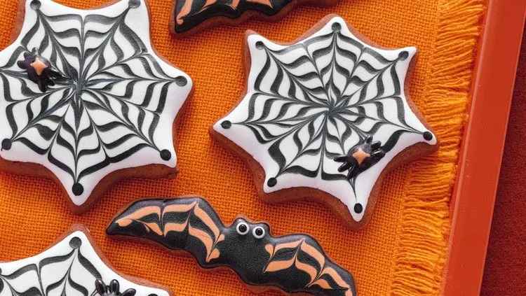 Martha Stewart bat and cobweb Halloween cookies decorated with black and white royal icing on an orange cloth
