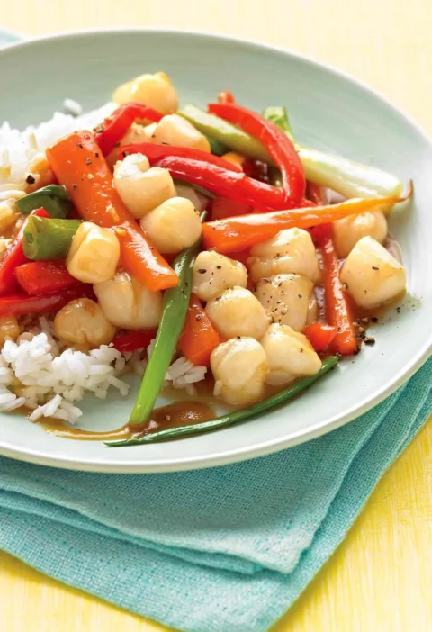 Martha Stewart bay scallop stir-fry with red bell pepper, carrots and scallions in a glossy sauce over white rice on a pale green plate