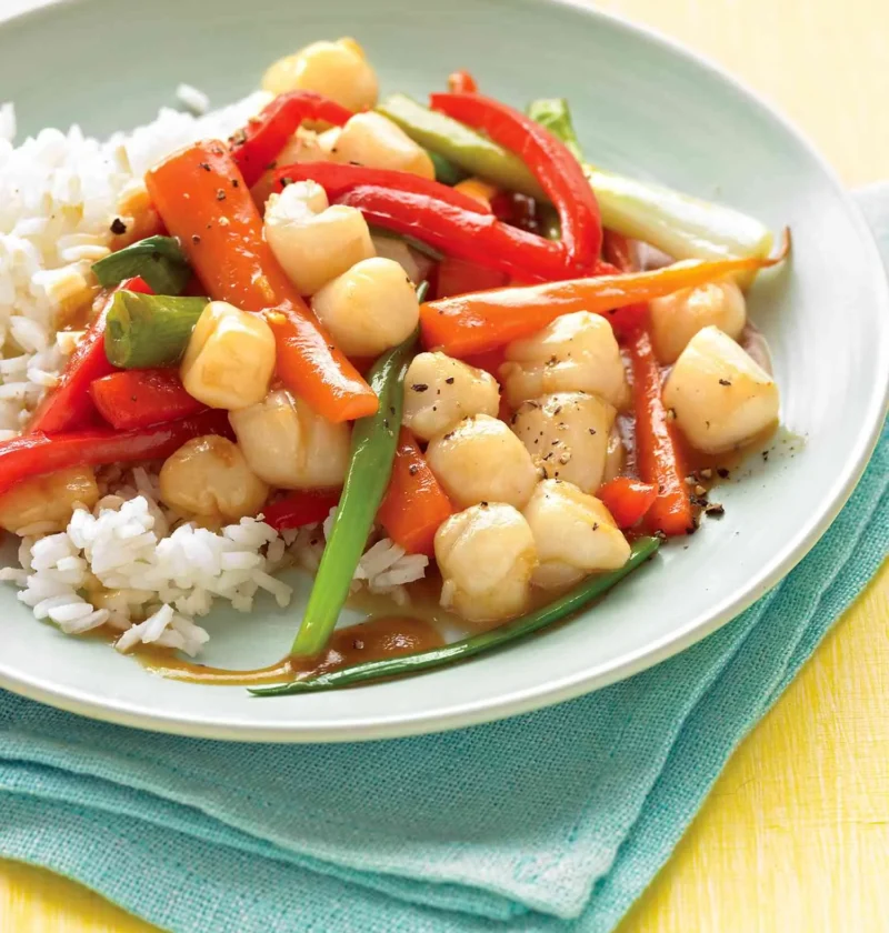 Martha Stewart bay scallop stir-fry with red bell pepper, carrots and scallions in a glossy sauce over white rice on a pale green plate