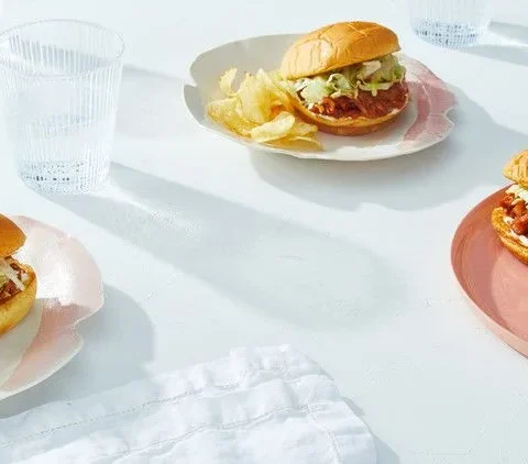 Martha Stewart BBQ jackfruit sandwich on a toasted potato bun with shredded lettuce, served with potato chips on plates