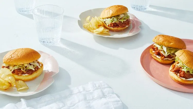 Martha Stewart BBQ jackfruit sandwich on a toasted potato bun with shredded lettuce, served with potato chips on plates