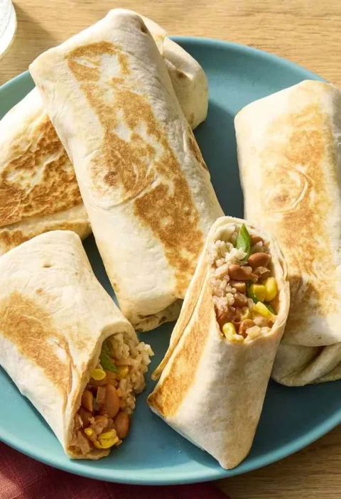 Martha Stewart bean burritos toasted golden on a teal plate, one cut open to show rice, pinto beans and corn, with salsa and sour cream