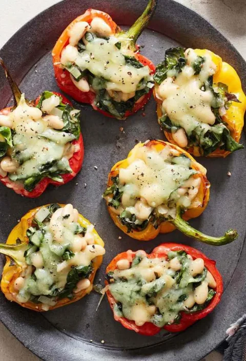 Martha Stewart beans-and-greens-stuffed peppers with melted fontina over Swiss chard and white beans on a dark oval platter