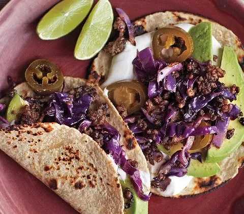 Martha Stewart beef and cabbage tacos with browned beef, purple cabbage, avocado, sour cream and pickled jalapenos on toasted tortillas with lime wedges