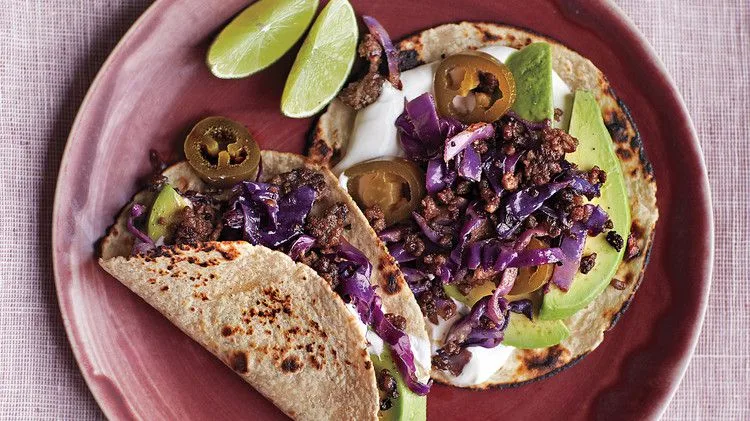 Martha Stewart beef and cabbage tacos with browned beef, purple cabbage, avocado, sour cream and pickled jalapenos on toasted tortillas with lime wedges