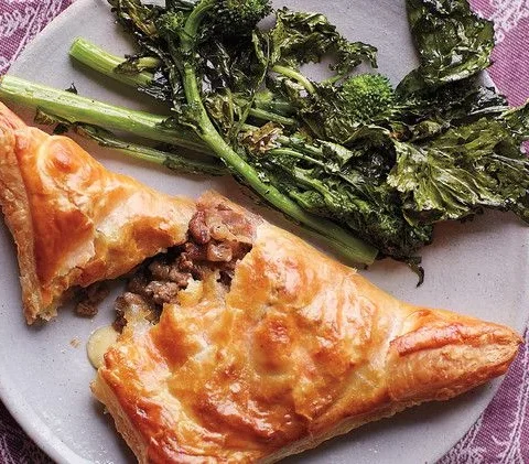 Martha Stewart beef and cheddar hand pies golden puff pastry triangle cut open to show beef filling beside roasted broccoli rabe
