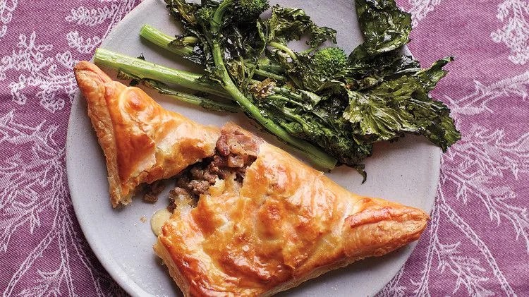 Martha Stewart beef and cheddar hand pies golden puff pastry triangle cut open to show beef filling beside roasted broccoli rabe